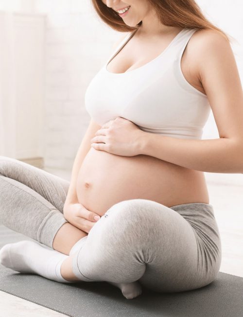 Workout, fitness and pregnancy concept. Young pregnant woman holding her stomach, sitting on floor in sport centre, panorama with empty space